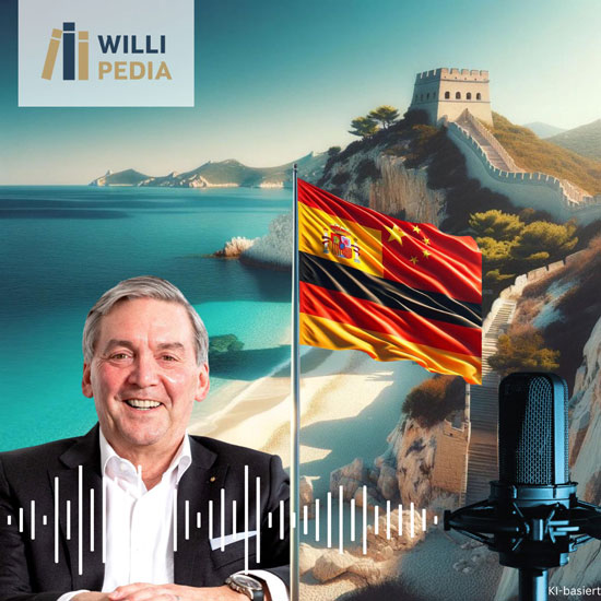 Thomas Meyer mit lilanem Jacket, im Hintergrund eine Bucht am Meer mir türkisem Wasser und Burg auf dem Berg. Neben ihm weht eine Flagge mit Spanischen und Deutschen Farben