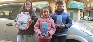 Drei Kinder stehen glücklich mit Geschenken vor einem Auto